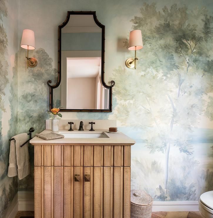 Elegant, whimsical bathroom is covered in hand painted wallpaper lit by