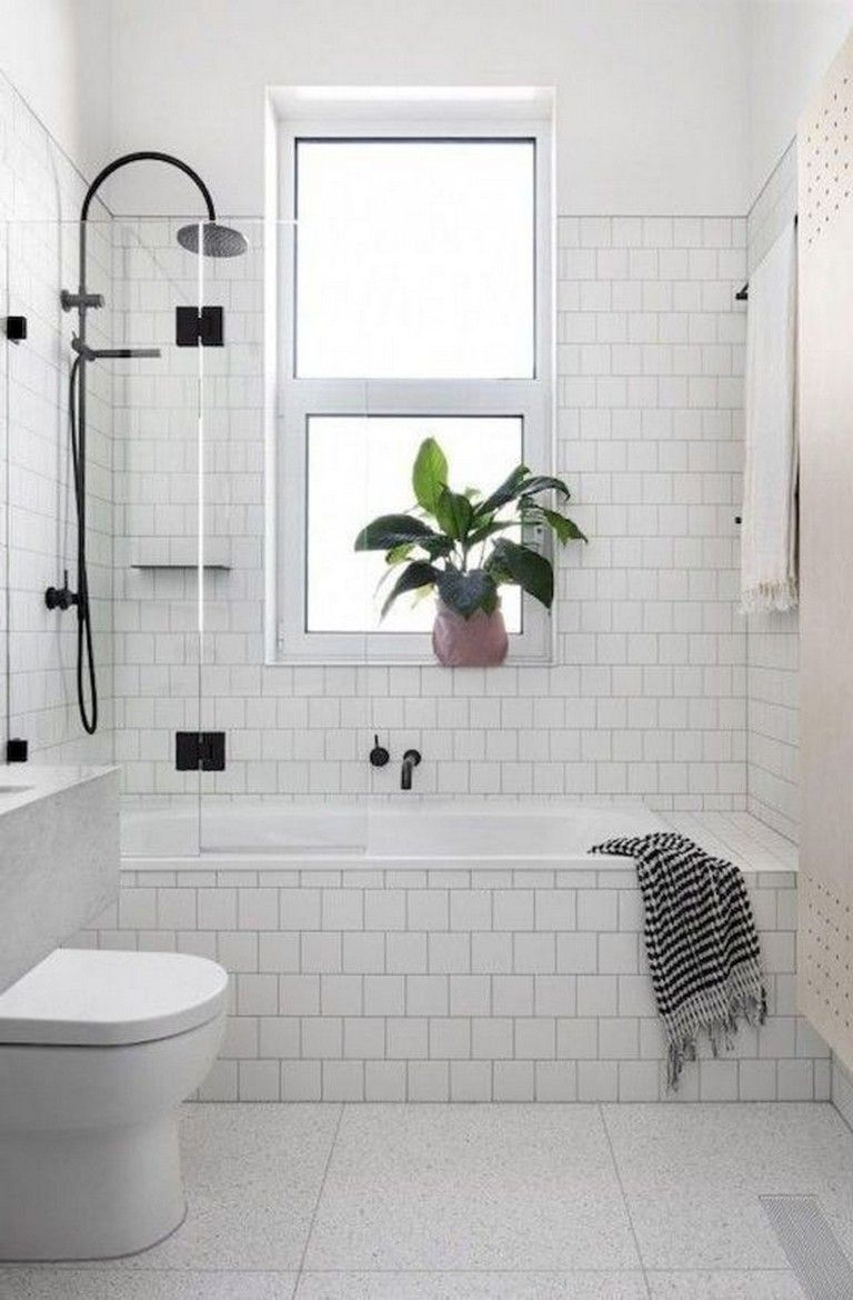 a white tiled bathroom with a toilet, bathtub and window in the corner