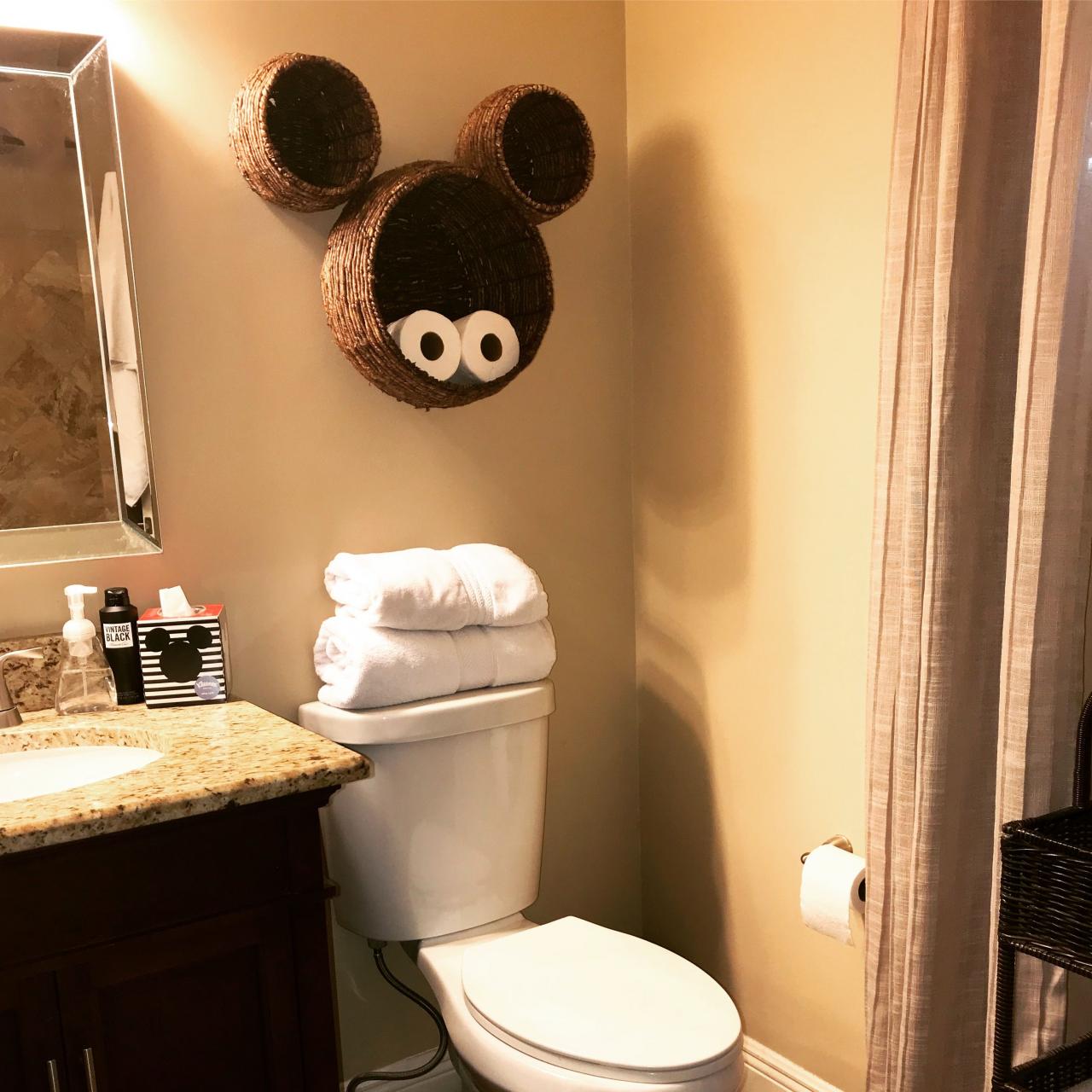 a bathroom with a toilet, sink and mickey mouse head on the wall above it